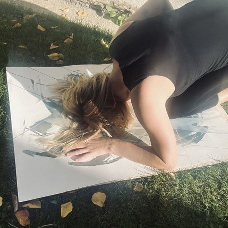 photographic bodyscape - live n°3 Frau in schwarzem Outfit liegt mit dem Kopf nach unten auf einer Leinwand im Freien.