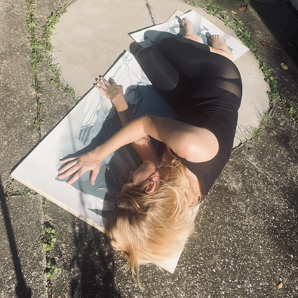 photographic bodyscape - live n°1 Frau liegt auf einer Matte, bekleidet mit einem schwarzen Outfit, auf dem Bauch.